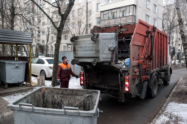  Сотрудник коммунальных служб выгружает мусор из контейнера в мусоровоз